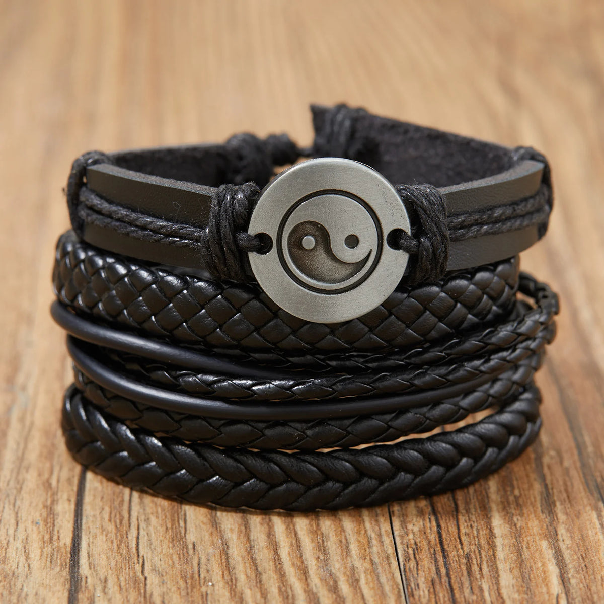 Stapel dunkelbrauner Lederarmbänder mit kreisförmigem Yin-Yang-Blatt-Anhänger.
