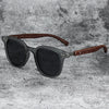 Gray sunglasses with dark lenses and brown wood grain frames resting on a gray textured surface.