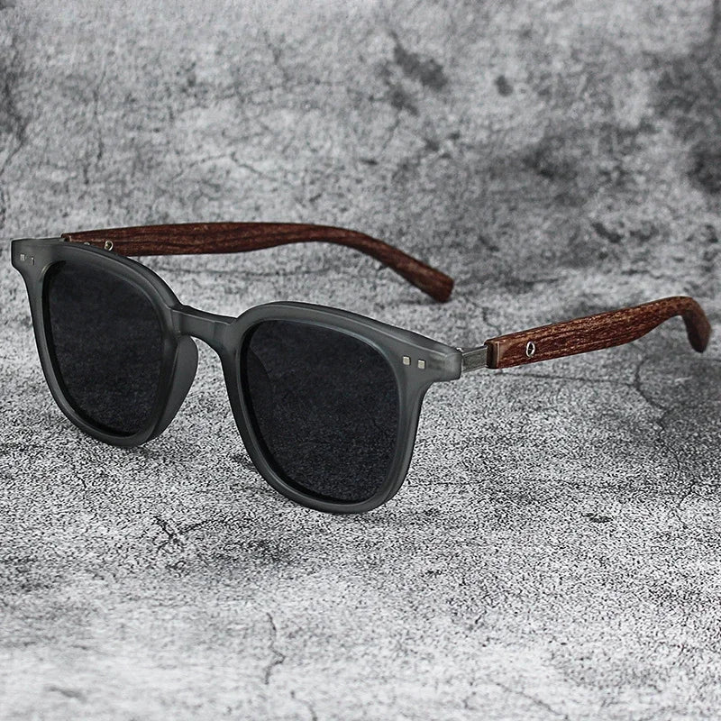 Gray sunglasses with dark lenses and brown wood grain frames resting on a gray textured surface.