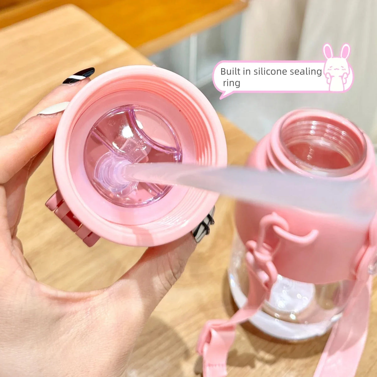 A hand is holding a pink silicone sealing ring and a water bottle, demonstrating the built-in sealing feature.
