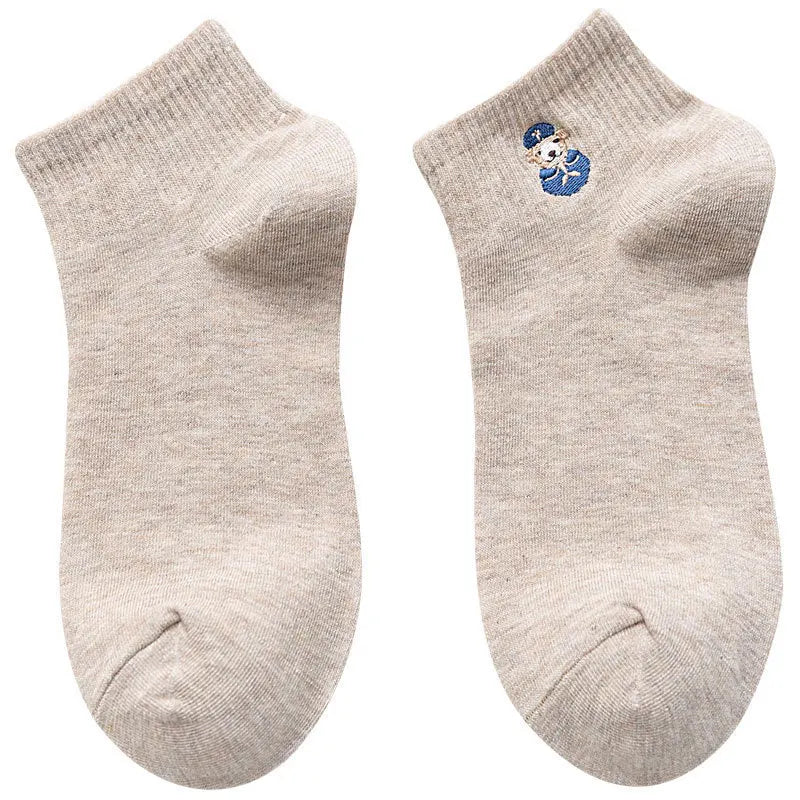 A pair of light beige cotton socks with a blue embroidered design on the toe.