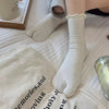 A close-up of white knit crew socks with ruffle cuffs worn on a foot, resting on a white fabric.