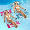 A woman wearing a white bikini floats on a blue pool with pink and teal inflatable pillows.