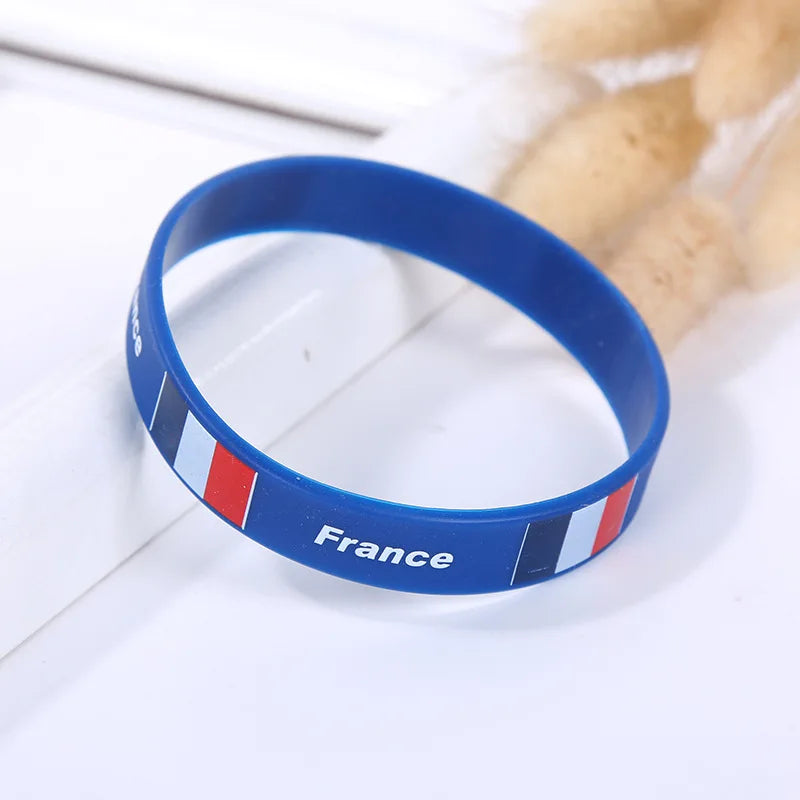 Blue silicone wristband with the French flag design resting on a white surface next to some light-colored objects.