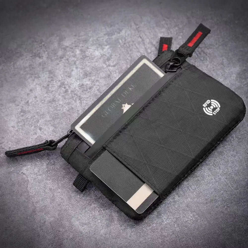 A black slim wallet with a clear card slot and RFID blocking features is shown on a gray surface.