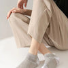 A person is shown wearing beige trousers and gray athletic knit ankle socks.