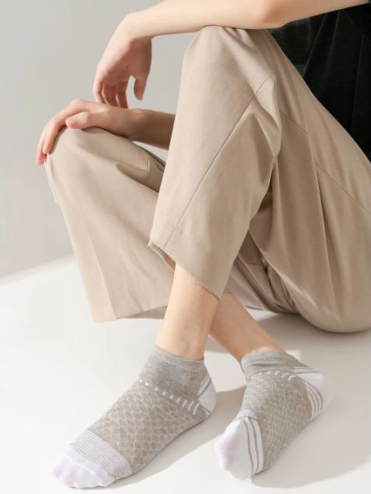 A person is shown wearing beige trousers and gray athletic knit ankle socks.