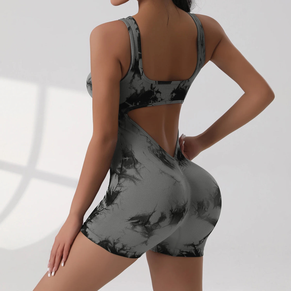 A woman wearing a tie-dye sport jumpsuit with a deep V-neck and cutout detail, shown from the back.