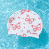 A white silicone swimming cap with a pink butterfly print floating in clear blue water.