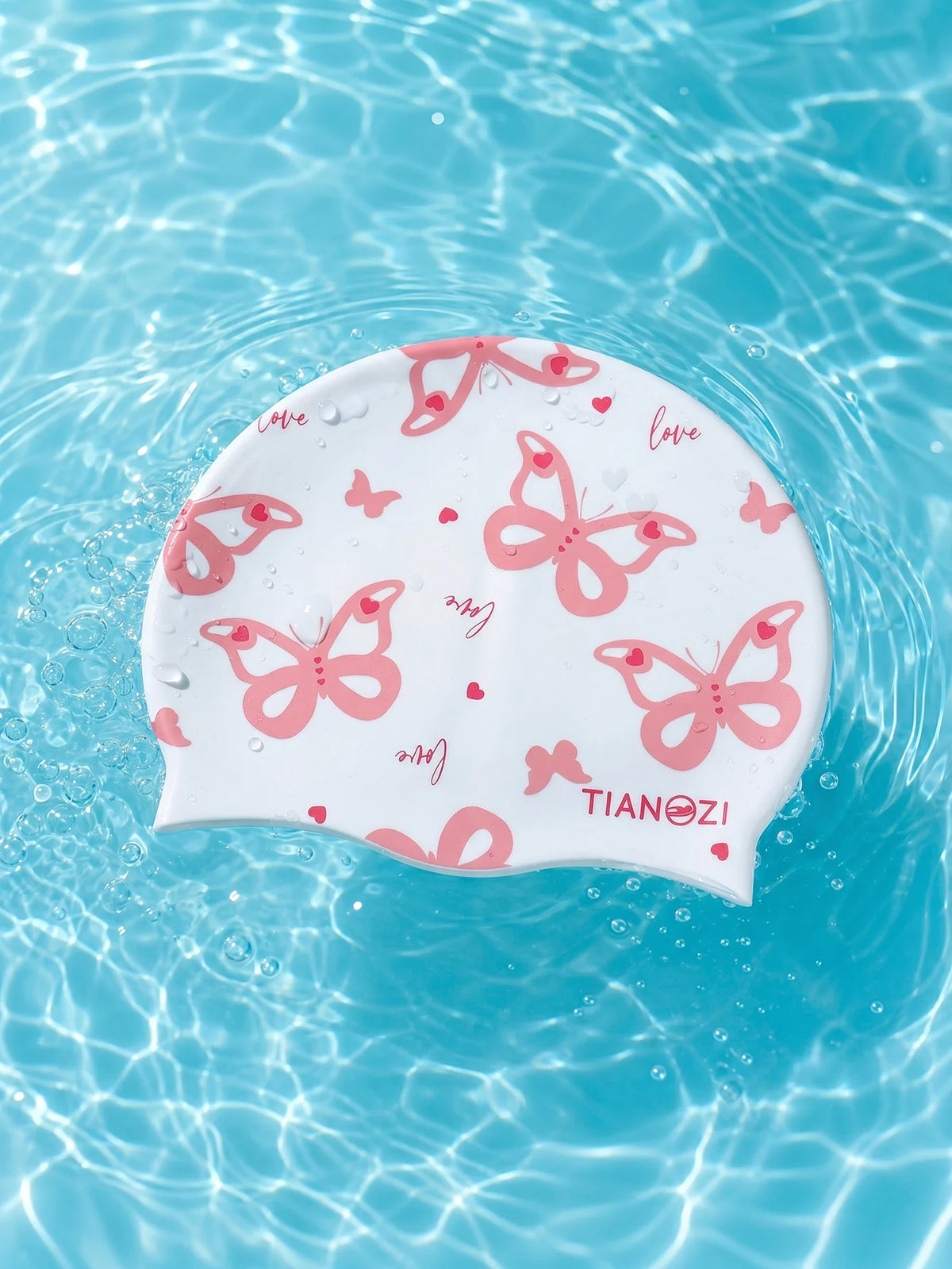 A white silicone swimming cap with a pink butterfly print floating in clear blue water.