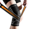 Black adjustable sports knee pads with orange directional arrows wrapped around a person's leg.