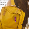 A yellow backpack with a purple whistle keychain attached to the strap.