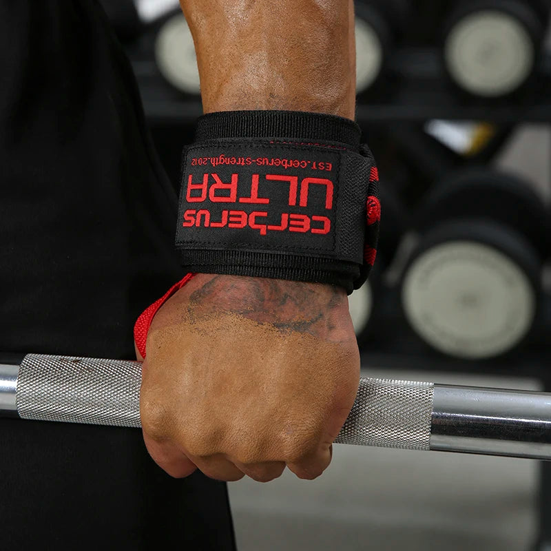 Gros plan d'une main agrippant une barre avec des sangles de poignet de musculation noires et rouges.
