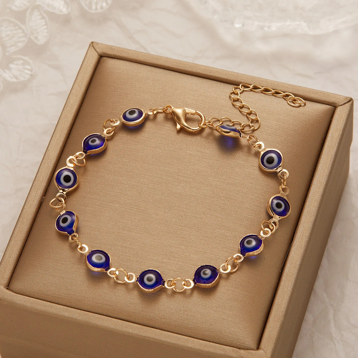 Gold charm bracelet with blue evil eye beads presented in a light brown box.