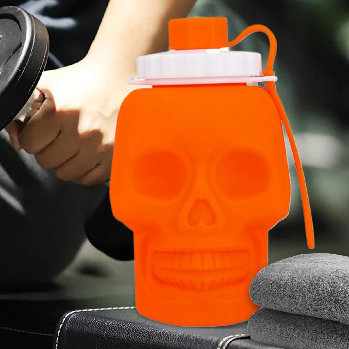 An orange skull-shaped leakproof sports water bottle with a clear cap and orange straw is held by a hand.