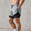 A man wearing gray quick-dry athletic shorts with black lining and a drawstring, standing against a concrete wall.