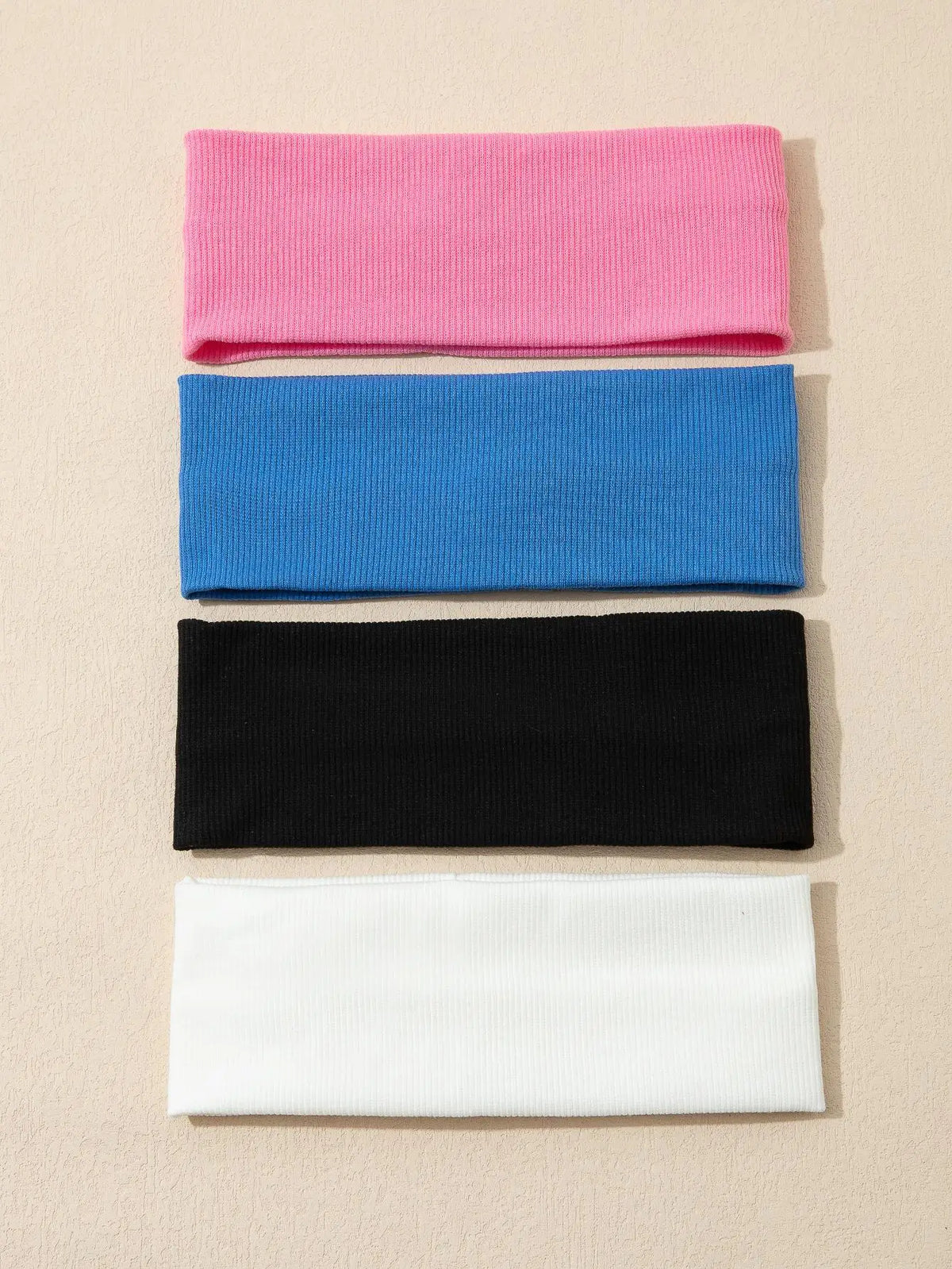 Un paquete de cuatro bandas elásticas para el cabello en rosa, azul, negro y blanco apiladas verticalmente.