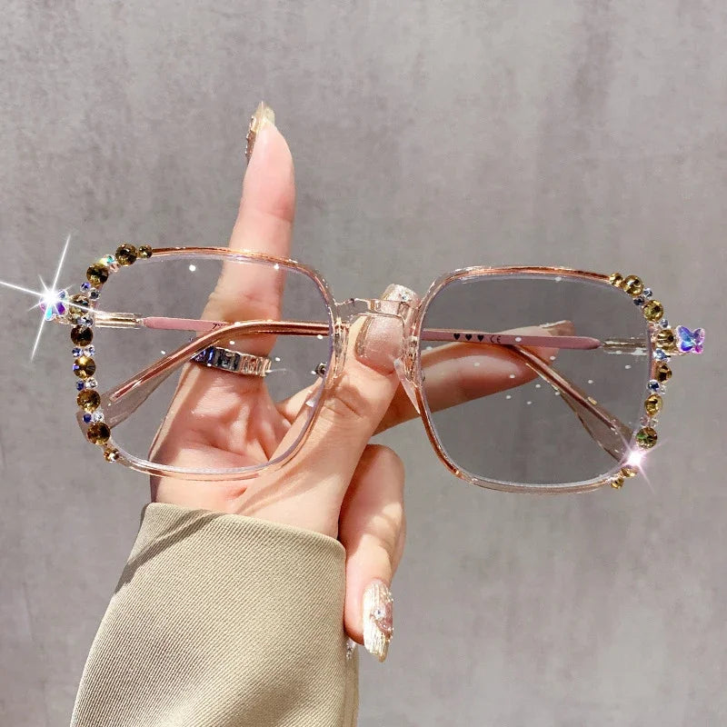 A hand holds a pair of pink photochromic diamond style eyeglasses adorned with small sparkling stones.