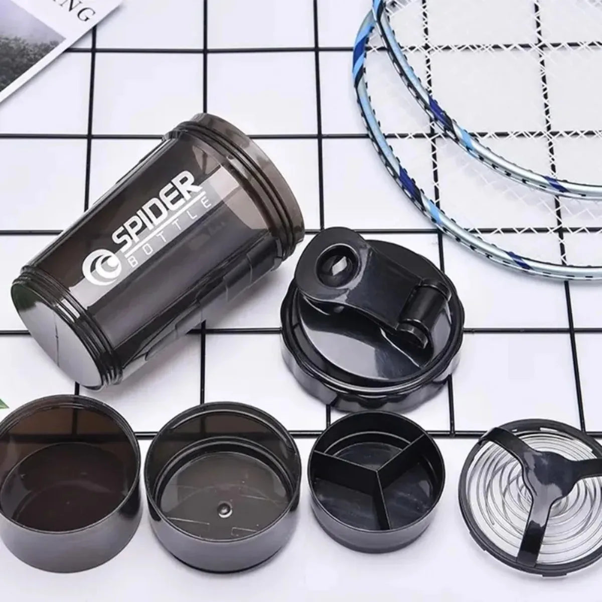 A black leak-proof protein shaker bottle with an attached pill tray and a mesh workout net.