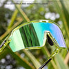 A pair of clear, large wide-angle photochromic cycling sunglasses are shown against a blurred green outdoor background.