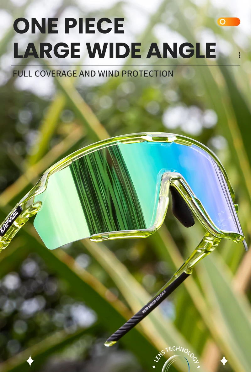 A pair of clear, large wide-angle photochromic cycling sunglasses are shown against a blurred green outdoor background.