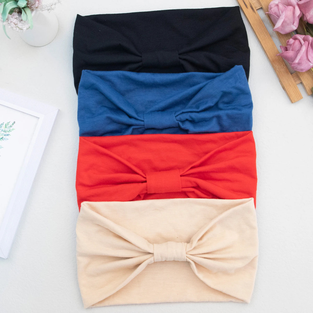 Ein Stapel von vier weichen elastischen breiten Stirnbändern in schwarz, blau, rot und beige.