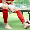 Eine Person trägt rote atmungsaktive Fußballstutzen und sitzt auf einem grünen Feld.