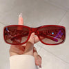 A hand holds a pair of red tinted Y2K cat eye rhinestone sunglasses against a light background.