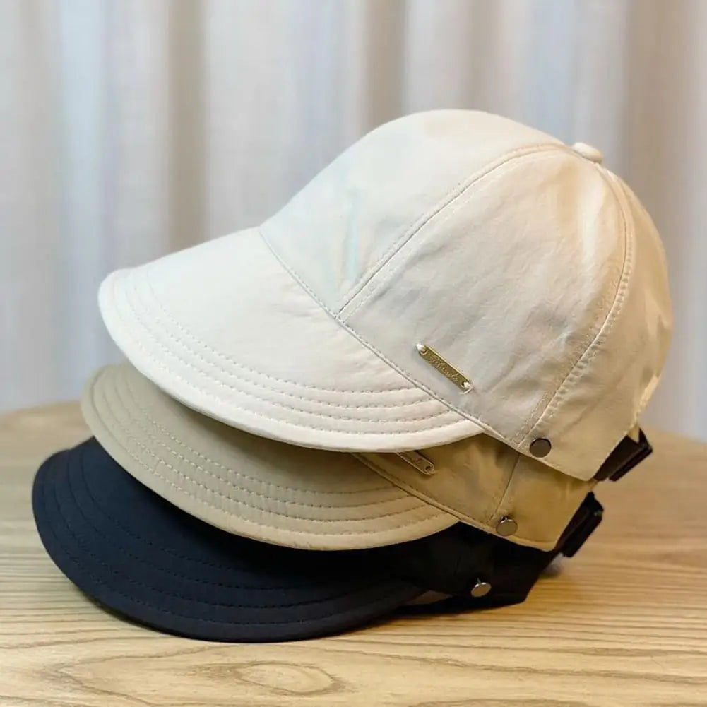 Gorra de béisbol beige con ala ancha y protección UV apilada sobre una superficie de madera.