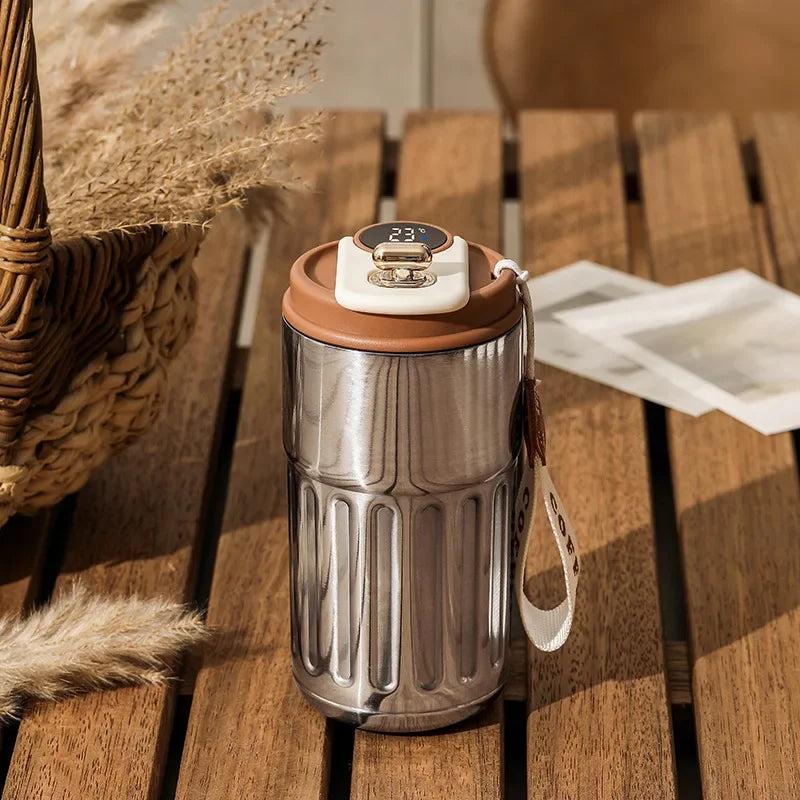 A stainless steel thermo mug with a white LED temperature display sits on a wooden surface.