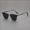 A pair of vintage square metal frame sunglasses with dark lenses resting on a gray surface.