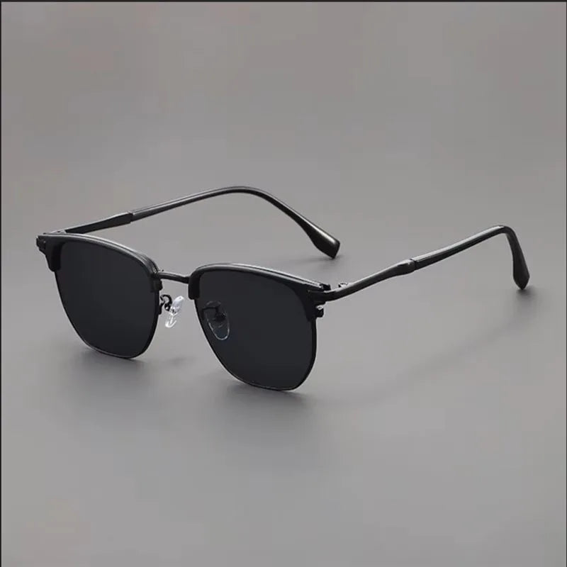 A pair of vintage square metal frame sunglasses with dark lenses resting on a gray surface.