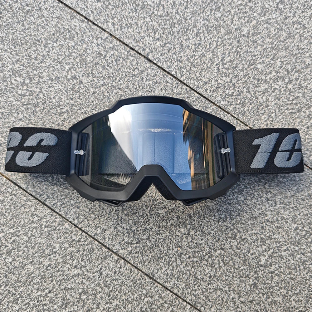 Une paire de lunettes de moto tout-terrain et ATV noires posées sur une surface grise texturée.