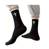 A pair of black knit mid-calf sports socks with a white cross design, shown on a person's leg.