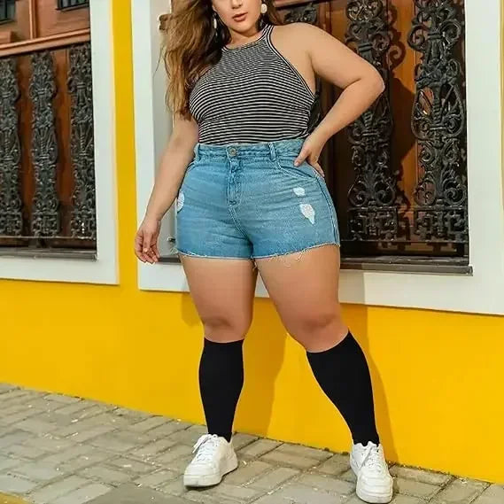 A woman wearing a striped top and denim shorts with black compression socks standing outdoors.