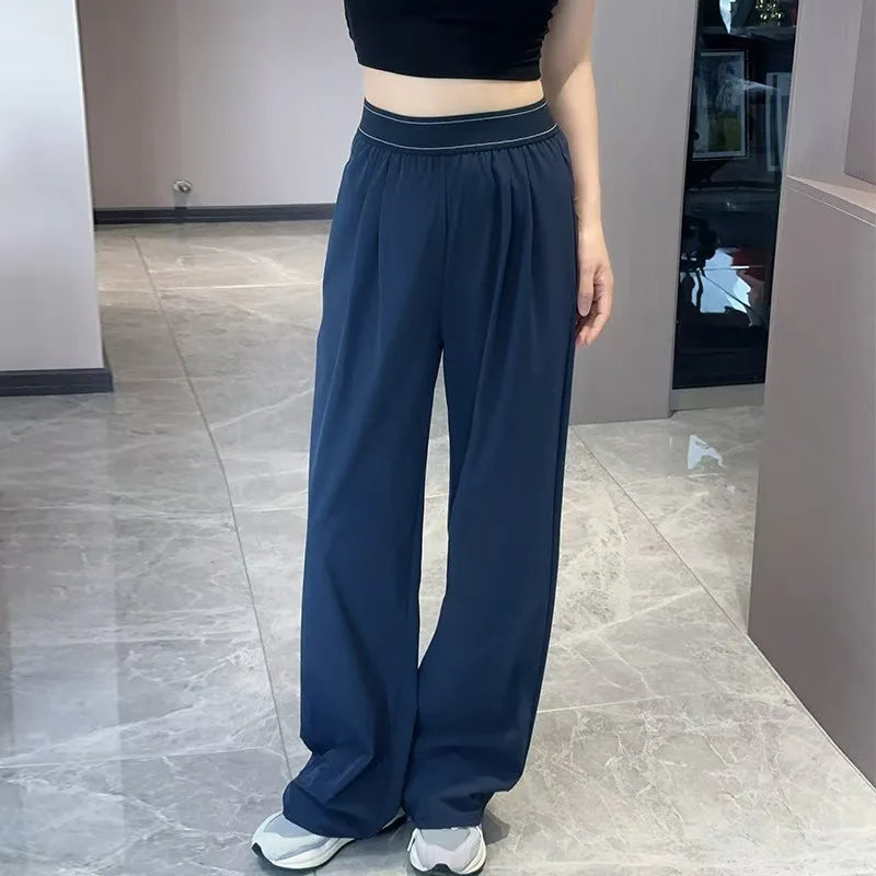 A woman wearing dark navy loose sports yoga pants and a black top standing indoors.