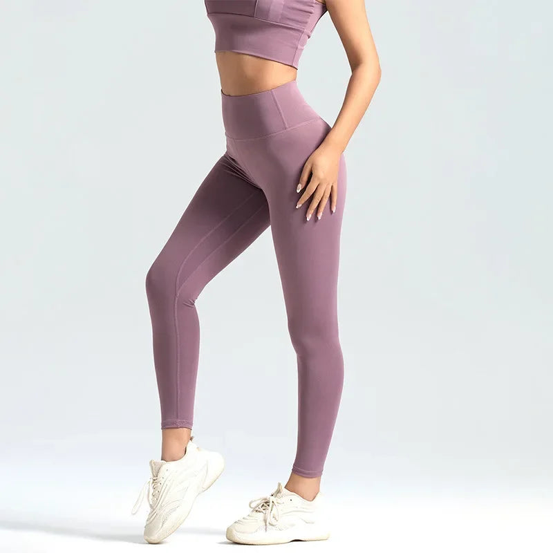 A model wearing seamless high-waist yoga leggings in mauve purple and a matching crop top, standing and posing.