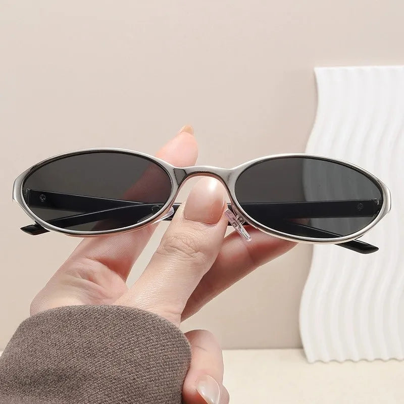 A hand holds a pair of black retro oval sunglasses with a silver metal frame against a white background.