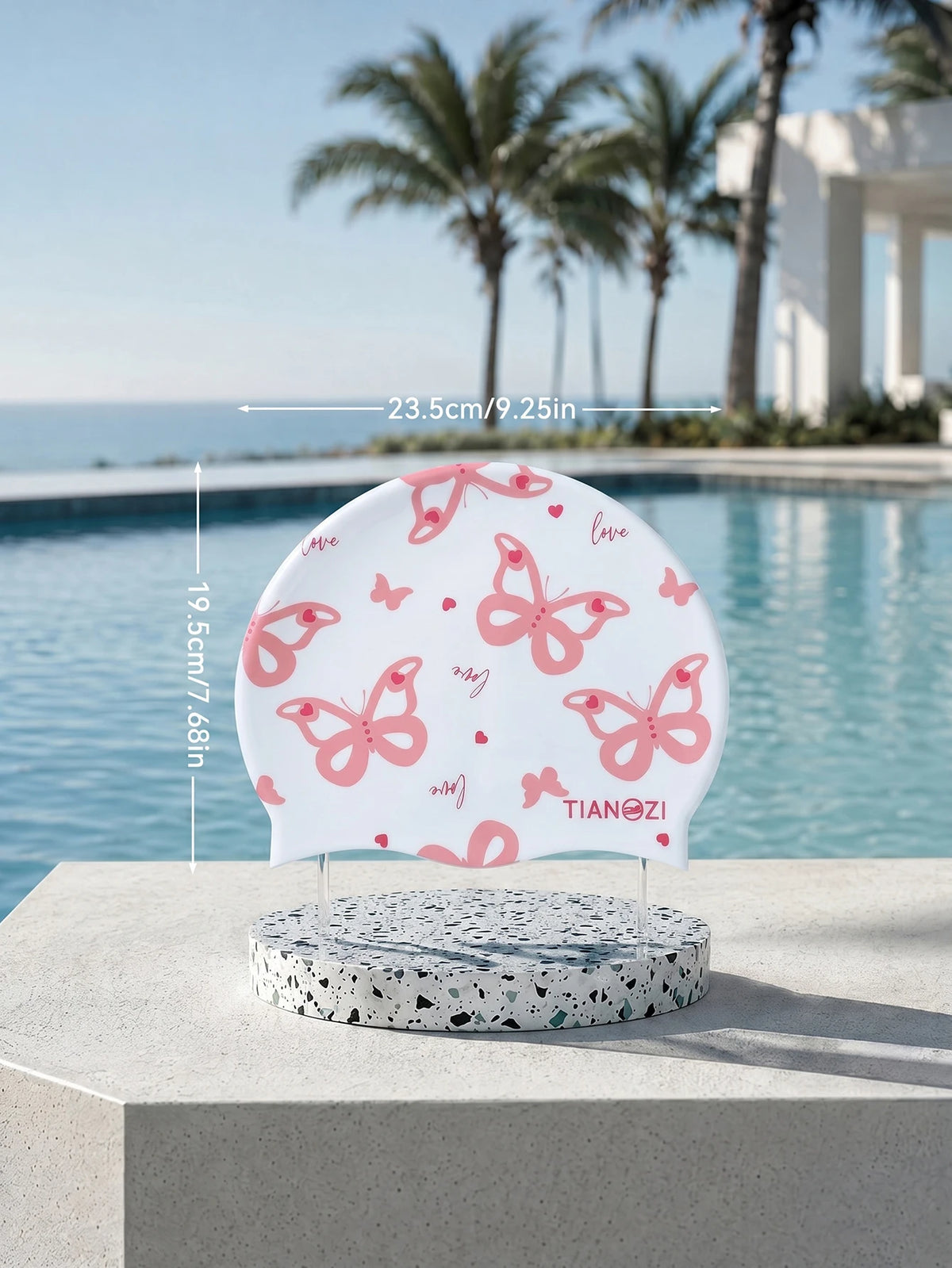White silicone swimming cap with pink butterfly print resting on a concrete surface by a pool.