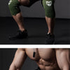 Muscular man wearing black athletic shorts and green compression knee sleeves, posing for a fitness photo.