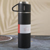 A black vacuum flask with a black handle and silver accents is standing on a dark surface.