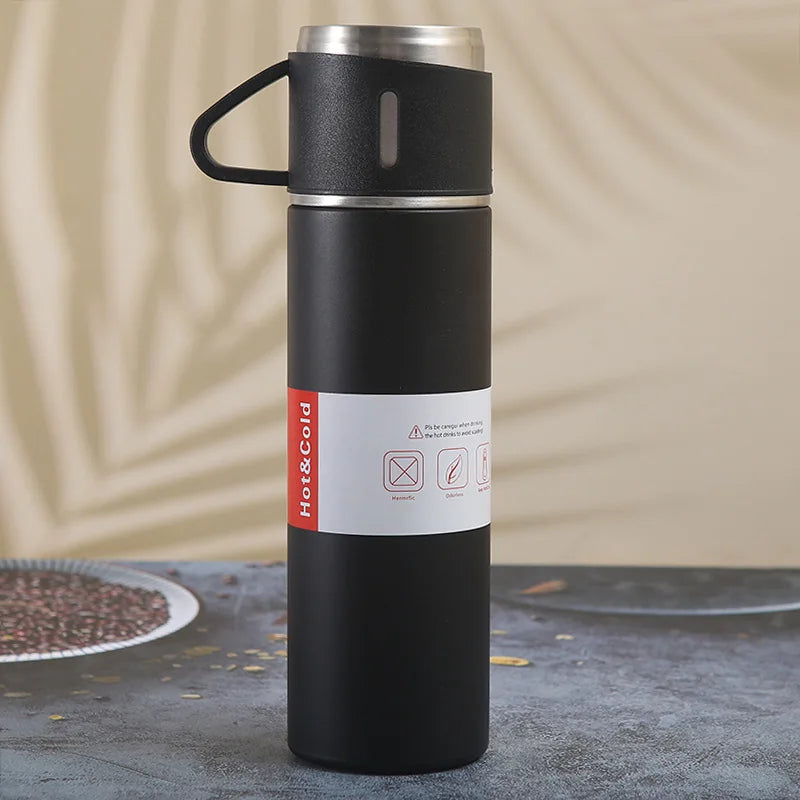 A black vacuum flask with a black handle and silver accents is standing on a dark surface.
