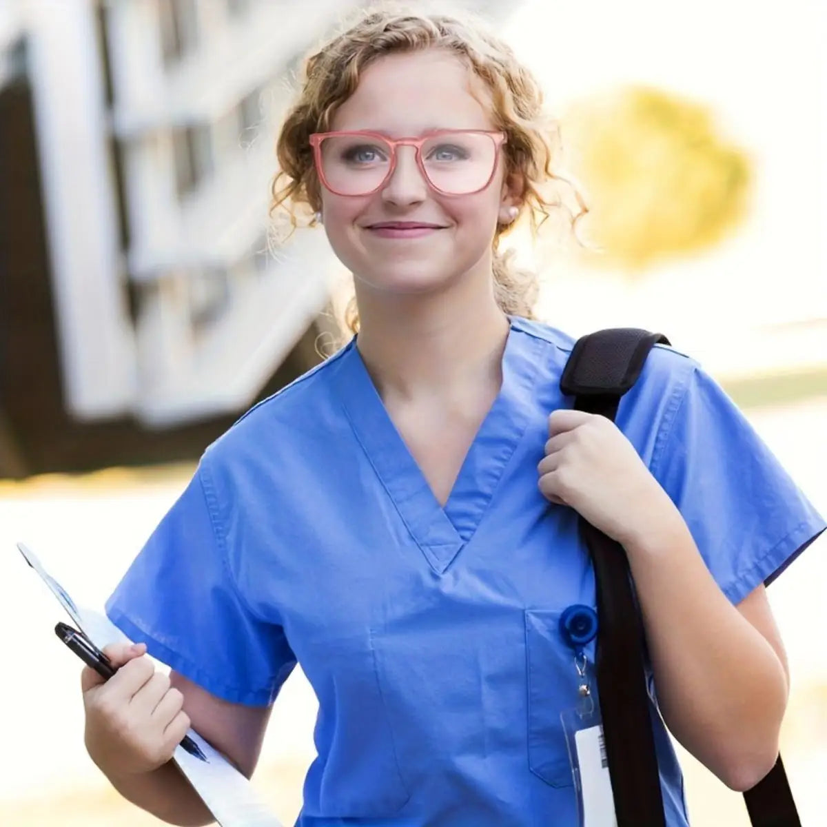 Eine junge Frau mit pinken Rahmen und klaren Schutzbrillen sowie einem blauen medizinischen Schürzenhemd.