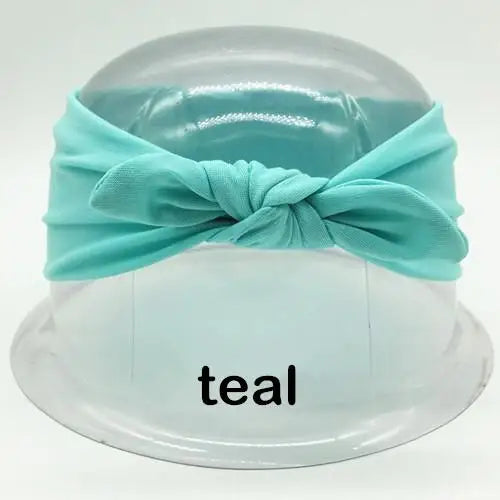Türkisfarbene Stoff-Haube, gebunden mit einer Schleife, auf einem klaren Plastikblech präsentiert.