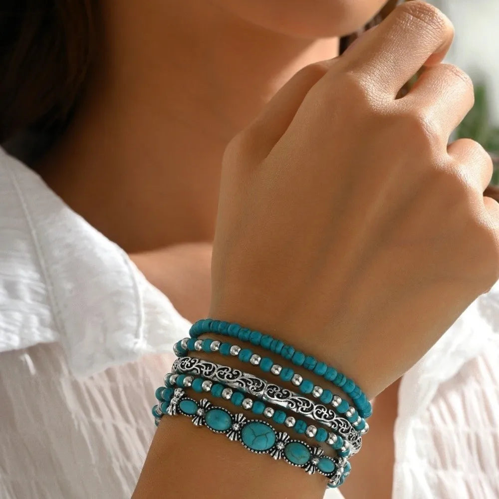 Gros plan d'une main portant une pile de bracelets en perles turquoise sur un poignet, contre un t-shirt blanc.