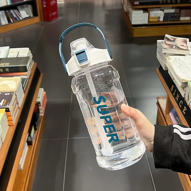 A hand holds a clear insulated sports water bottle with a blue lid and straw against a blurred background of bookshelves.