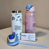 A pink and white vacuum insulated water bottle with a straw and a blue lid, next to an empty stainless steel bottle and a blu