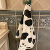 A white and black cow print face towel hanging on a tile backsplash.