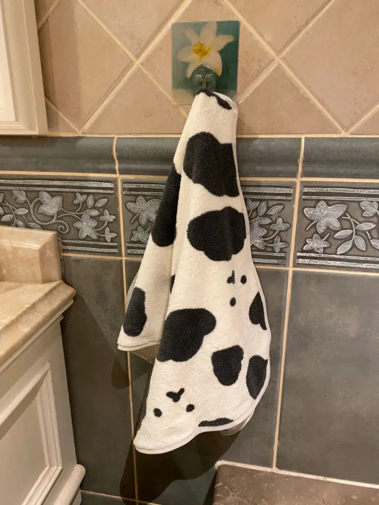 A white and black cow print face towel hanging on a tile backsplash.