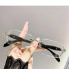 A hand holds a pair of frameless photochromic prescription glasses with blue light blocking features against a light gray bac